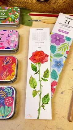 three tins with flowers on them sitting next to some scissors and other things in the background