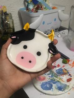 a hand holding a pig shaped plate on top of a table next to paintbrushes