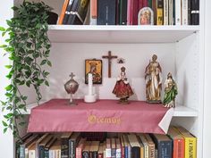 a shelf filled with books and figurines next to a cross on top of a table