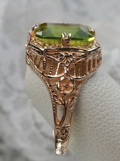 Natural Green Peridot 10k or 14k Rose Gold RingLovely Rectangle Design#D148 Make heads turn and stand out with this gorgeous piece of jewelry! This Edwardian reproduction filigree ring is made from rose gold and features an emerald cut high quality natural green Peridot gemstone measuring 9mm by 7mm. From the beautiful intricate floral daisy design to the inside of the band marked 10K or 14K for gold – this ring will take your look to the next level! Look no further than this exquisite vintage-i Yellow Gold Peridot Jewelry With Emerald Cut, Gold Peridot Jewelry With Emerald Cut, Elegant Rectangular Peridot Rings, Emerald Cut Peridot Jewelry For Formal Occasions, Emerald Cut Peridot Jewelry For Formal Events, Formal Emerald Cut Peridot Jewelry, Victorian Style Gold Jewelry With Emerald Cut, 14k Gold Green Rings With Intricate Design, Elegant Rectangular Peridot Jewelry