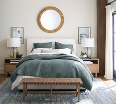 a bedroom with a bed, nightstands and round mirror on the wall above it