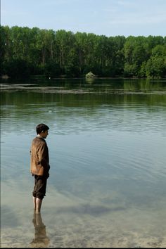 a man standing in shallow water looking at trees