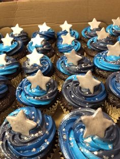 cupcakes with blue frosting and silver stars on them in a cardboard box