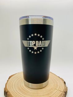 a black tumbler cup with the words top dad on it sitting on a tree stump