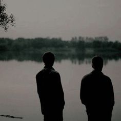 two people standing next to each other in front of a body of water on a foggy day