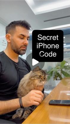 a man sitting at a table holding a cat and looking at his cell phone with the caption'secret iphone code '