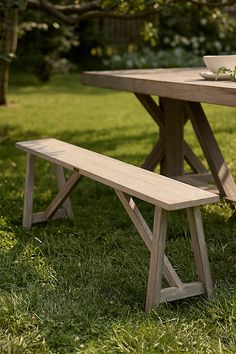 a picnic table with a bowl of salad on it and a bench in the grass