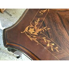 an ornate wooden table with gold leaf designs on the top and bottom, sitting on a marble floor