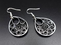 two pairs of silver earrings on a black surface, one with swirls and the other has