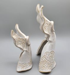 two white porcelain figurines sitting next to each other on a gray surface,