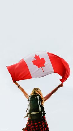 a woman holding a canadian flag while standing on top of a hill with her hands in the air