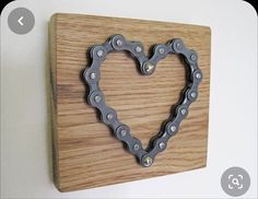 a heart shaped bicycle chain on a wooden plaque mounted to a wall with a white background