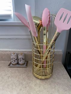 pink utensils are in a gold cup on the counter next to two salt shakers