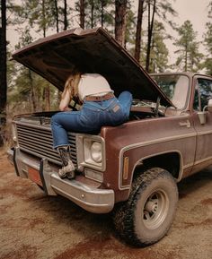 a woman sitting on the hood of an old pickup truck with her head in the open