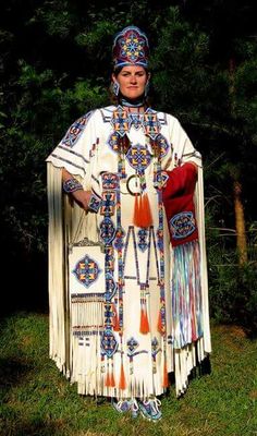 a woman dressed in native clothing standing on grass