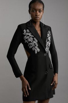 a woman in a short black dress with an embellished blazer and silver hoop earrings