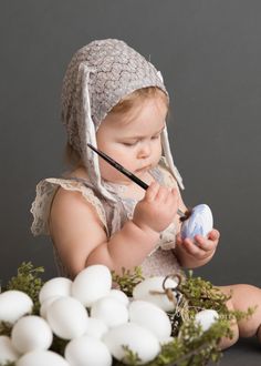 a baby is holding an easter egg and painting it with a watercolor brush while surrounded by white eggs