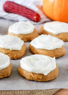 several cookies with frosting on top sitting on a piece of parchment paper next to a pumpkin