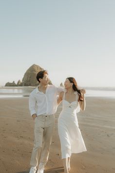 a man and woman are walking on the beach holding each other's hands as they look into the distance