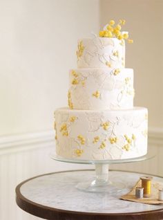 a white and yellow wedding cake on a small table with some gold flowers in the middle