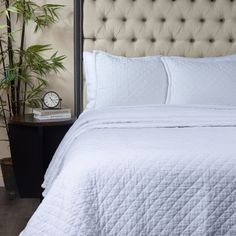 a bed with white sheets and pillows next to a potted plant on a nightstand