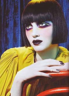 a woman with black and yellow makeup holding a red handle in front of her face