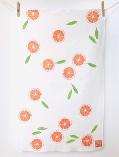 an orange print tea towel hanging on a clothes line with green leaves and slices of oranges