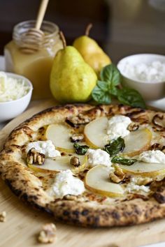 a pizza sitting on top of a wooden cutting board next to bowls of cheese and pears