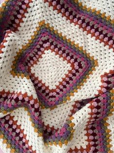 a crocheted blanket that is laying on top of a pink and white table