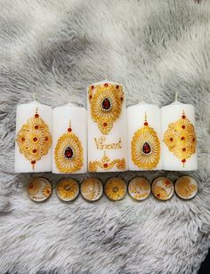 four white candles with gold designs on them sitting next to each other in front of a fur rug