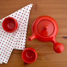 a red tea set on top of a wooden table next to a white polka dot napkin