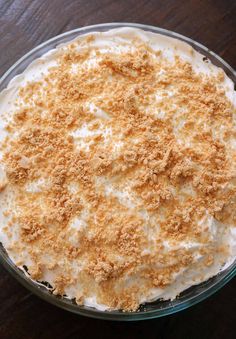 a pie with white frosting and crumbs in a glass dish on a wooden table