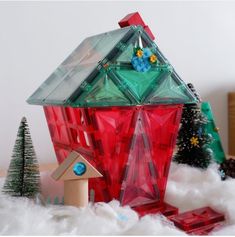 a red glass birdhouse sitting on top of snow covered ground next to christmas trees