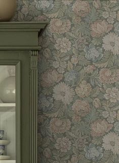 a green cabinet with flowers on it next to a wallpapered wall in a room