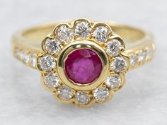 a yellow gold ring with an oval ruby and diamond center surrounded by smaller round diamonds