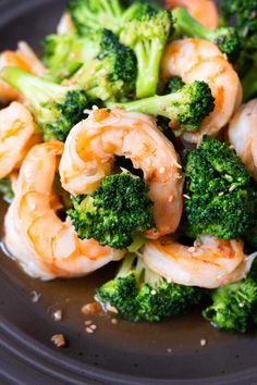 shrimp and broccoli on a black plate with sesame seed sprinkles