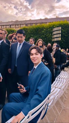 a man in a suit and tie sitting on a chair next to another man who is looking at his cell phone