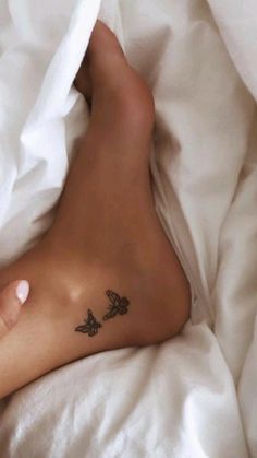 a person laying in bed with a tattoo on their left foot and butterfly tattoos on the lower leg