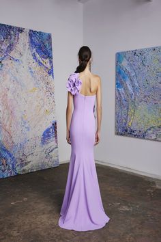 a woman standing in front of paintings wearing a purple dress with ruffles on the shoulders