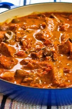 a blue pot filled with meat and sauce on top of a cloth covered tablecloth