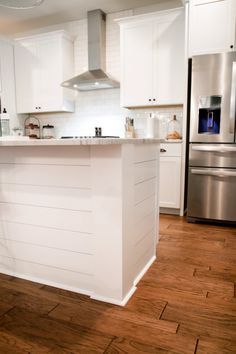 a kitchen with white cabinets and stainless steel appliances in the center, along with hardwood flooring