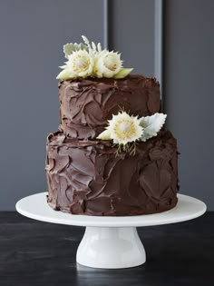 a three layer chocolate cake with white flowers on the top and bottom, sitting on a plate