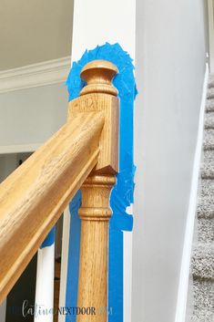 a wooden banister with blue tape on the wall behind it and stairs painted white