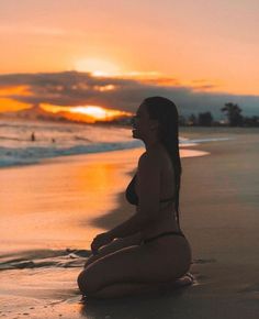 a woman is sitting on the beach at sunset