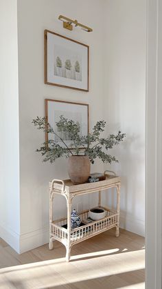 a white table topped with a potted plant next to a framed painting on the wall