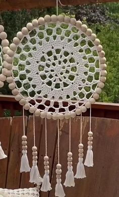 a white crocheted dream catcher hanging from a wooden fence with tassels