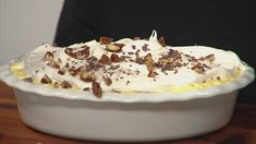 a dessert dish with white frosting and chopped nuts on the top, sitting on a wooden table