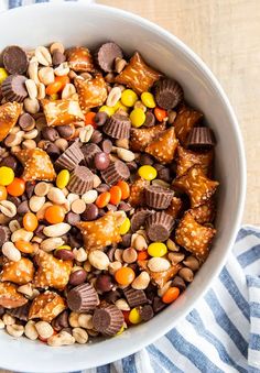 a white bowl filled with candy corn and chocolate covered pretzel treats on top of a blue and white striped towel