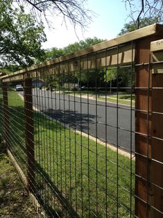 the fence is made of metal wire and has a wooden post at the top, along with green grass