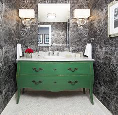 a bathroom with marble walls and green dresser in the corner, along with two framed pictures on the wall